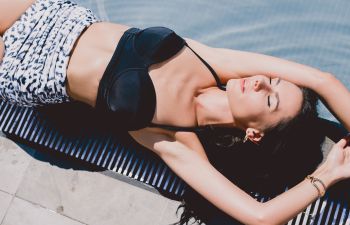 Slim brunette woman sunbathing by a swimming pool.